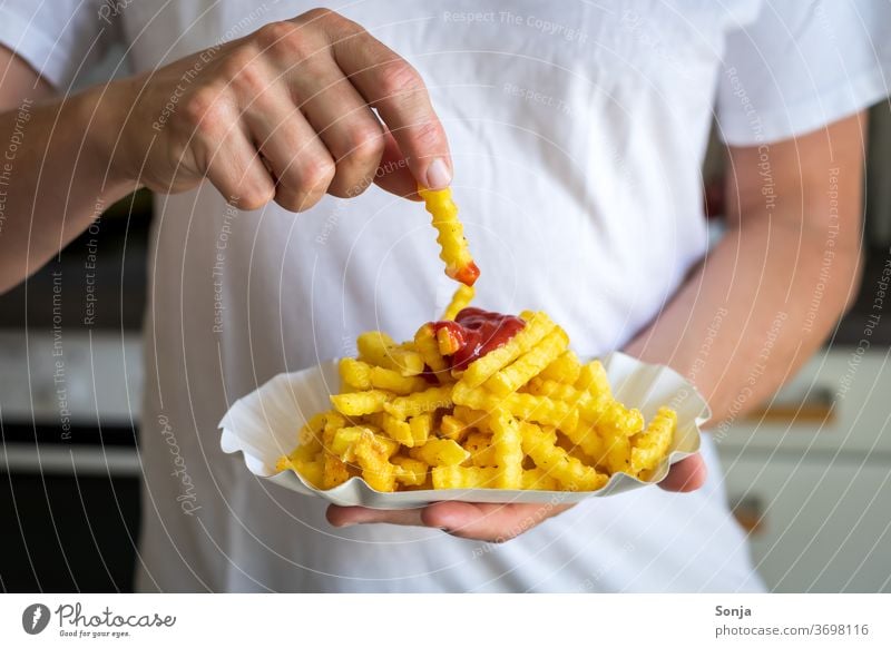 Mann tunkt ein Pommes Frittes in Ketchup Pommes frites Pappteller Hand tunken Küche Nahaufnahme Fett Fastfood Mittagessen ungesund Appetit & Hunger lecker