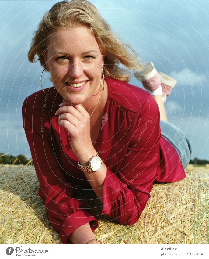 Junge Frau liegt auf einem Strohballen auf dem Feld und lächelt Freizeit Spaß Freude Jeans Ganzkörper Zentralperspektive Blick in die Kamera