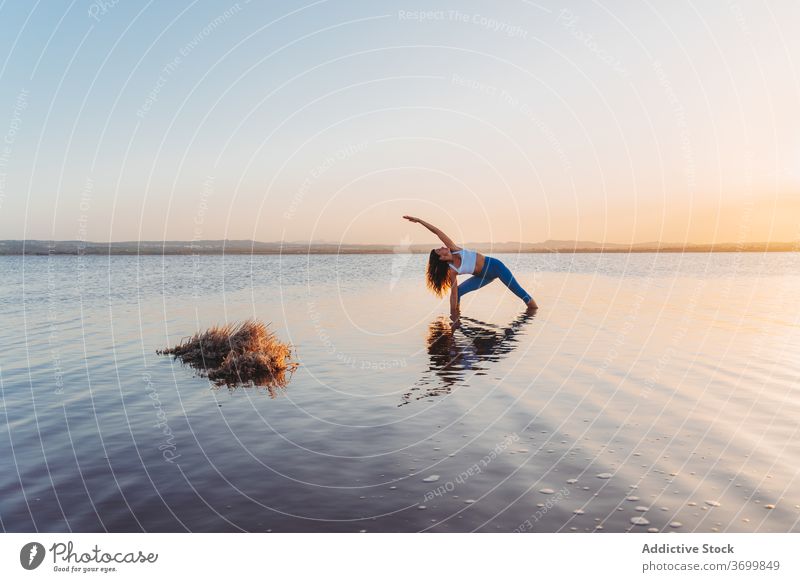 Frau in verlängerter Seitenwinkel-Pose, die sich im Seewasser spiegelt Yoga üben Asana utthita parsvakonasana stehen Harmonie Sprit Geist Anmut Fokus Wasser