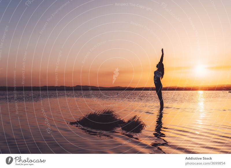 Fokussierte Frau mit erhobenen Armen übt Yoga im See Wasser üben Asana Pose stehen Aufwärtssalto Harmonie urdhva hastasana Gleichgewicht Windstille Wellness