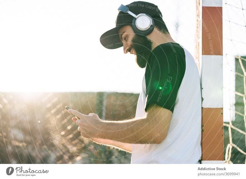Zufriedener Mann, der mit Kopfhörern Musik hört zuhören Hipster Smartphone Talkrunde soziale Netzwerke benutzend Sommer männlich Mobile Internet Anschluss