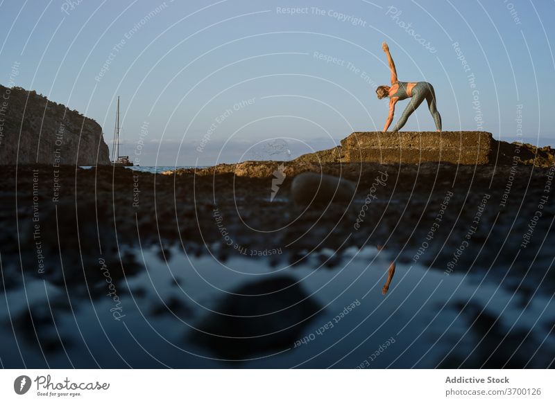 Unerkennbare Frau macht Yoga am Meer MEER üben Asana Pose gedrehtes Dreieck parivrtta trikonasana verdrehen Meeresufer stehen Harmonie Wellness Lifestyle Natur
