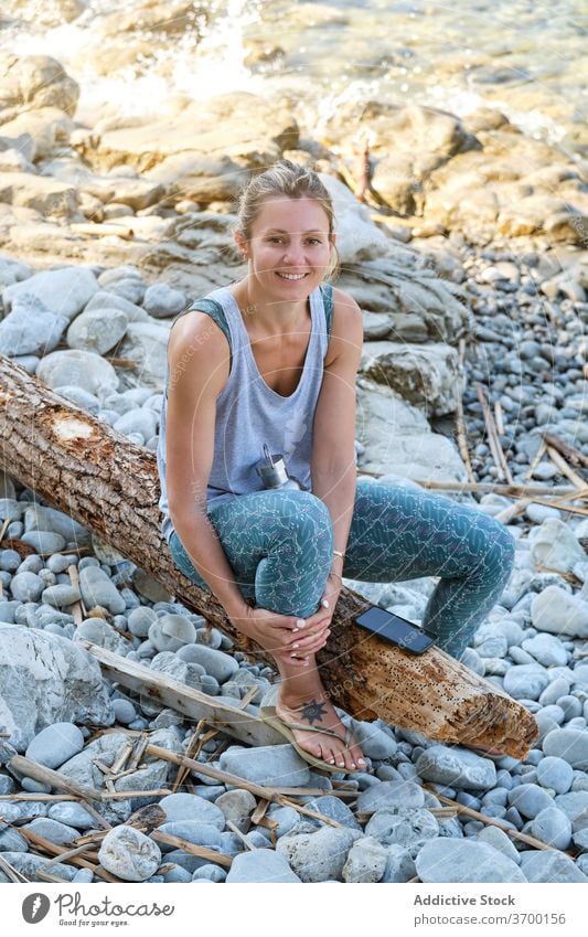 Sorglose Frau am steinigen Strand am Morgen felsig Meeresufer sich[Akk] entspannen Yoga Kälte Lächeln MEER Sportbekleidung Baum Kofferraum sitzen ruhen Glück