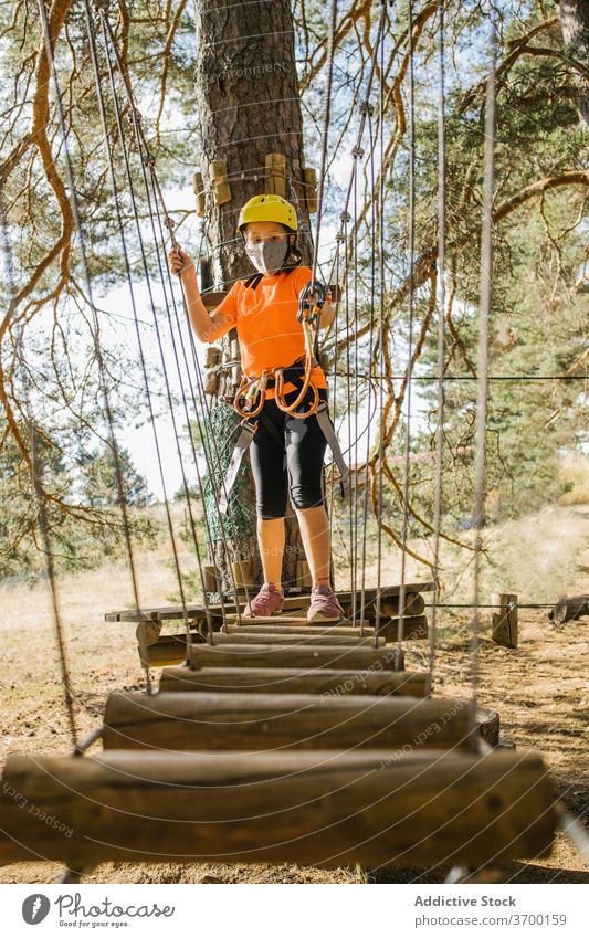 Kind hat Spaß im Abenteuerpark Park Brücke Suspension Sicherheit Gerät Kabelbaum Mundschutz Coronavirus Seil Karabiner behüten Spaß haben COVID Seuche