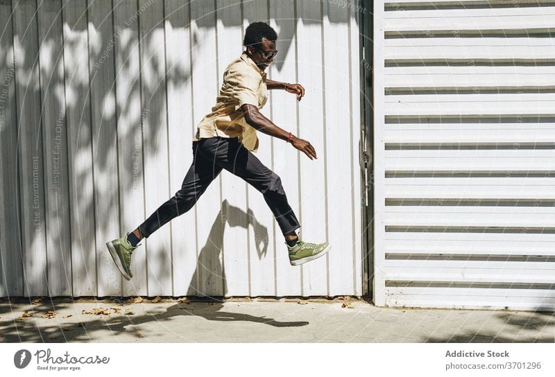 Fröhlicher ethnischer Mann springt auf der Straße sorgenfrei springen heiter Freiheit sonnig schlendern Großstadt Stil männlich schwarz Afroamerikaner Barcelona