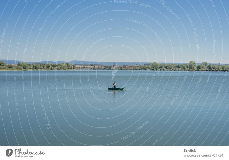 Ein einzelner  Angler in seinem Boot auf einem See Dorf Kirche ländlich blau Landschaft einsam still Stille Ortschaft Lothringen Kanal Wasser Horizont Ruhe
