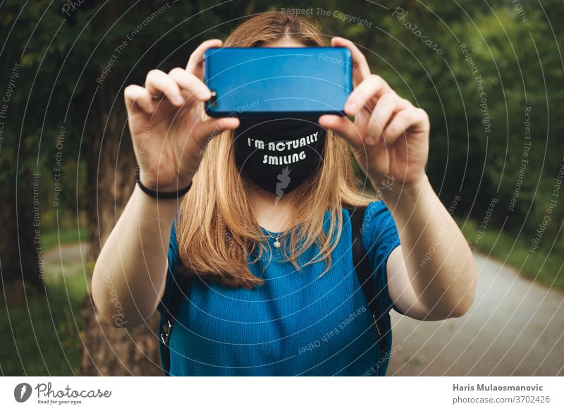 Frau hält Mobiltelefon in der Hand und bedeckt ihre Augen mit Maske im Freien lässig Konzept Korona-Technik Corona-Virus bedeckte Augen abgedeckte Fläche
