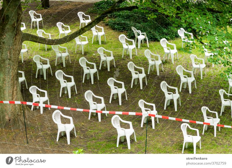 Die weißen Plastikstühle hatten sich im Park versammelt, natürlich unter Beachtung der Abstandsregel Plastikstuhl Absperrband grün Baum Corona Pandemie