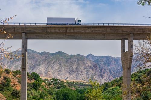 Lastwagen mit Kühlsattelanhänger überquert ein Viadukt mit einer Berglandschaft im Hintergrund Brücke Straße gekühlt Berge trayler Transport Verkehr Autobahn