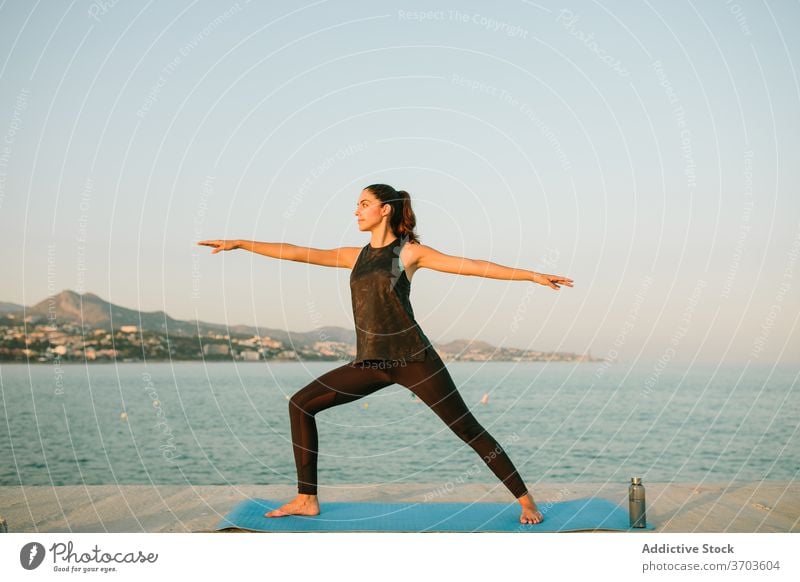Ruhige Frau in Warrior Pose auf Yoga-Matte Krieger-Pose virabhadrasana Windstille üben MEER Barfuß Unterlage Sportbekleidung ruhig erstaunlich Meereslandschaft