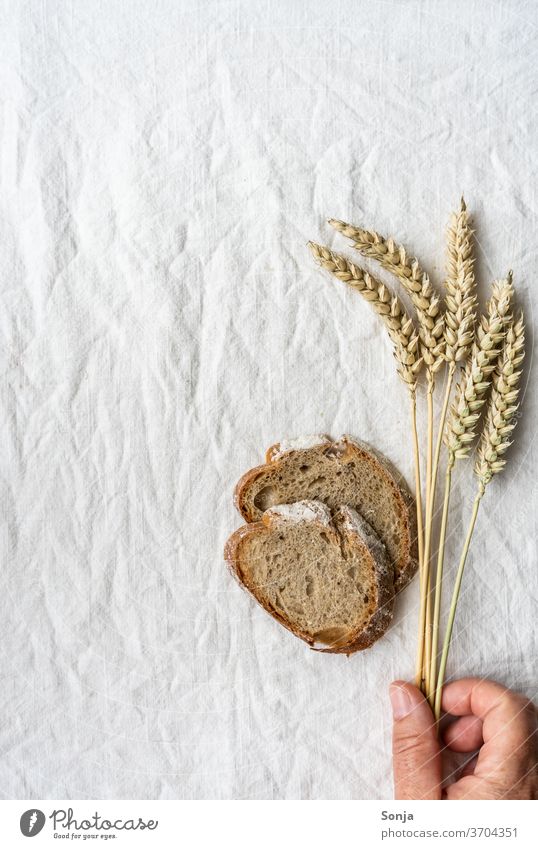Hand mit Weizenähren und zwei Scheiben Brot auf einem Leinen Tischtuch. Draufsicht. Brotscheibe halten Leinentuch Gesunde Ernährung Bioprodukte Frühstück