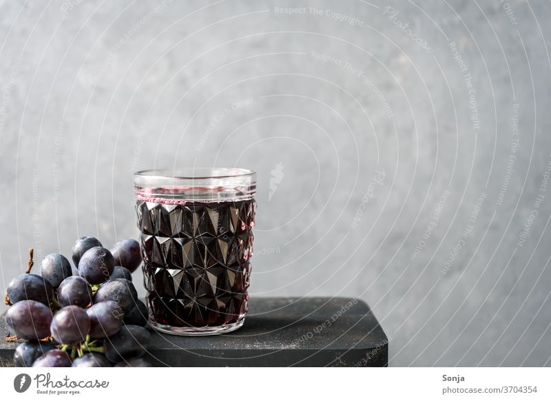 Frischer Traubensaft in einem Glas und blaue Weintrauben auf einem grauen Hintergrund Getränk Frucht Alkohol Rotwein rot Lebensmittel Stil Hintergrundbild