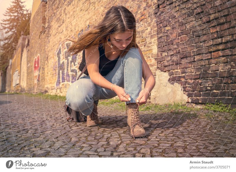 junge Frau in Sommerkleidung bindet ihre Schuhe hockend Straße im Freien schön konzentriert Tasche Wand Baustein Berlin Lifestyle Straßenbelag Teenager Mädchen