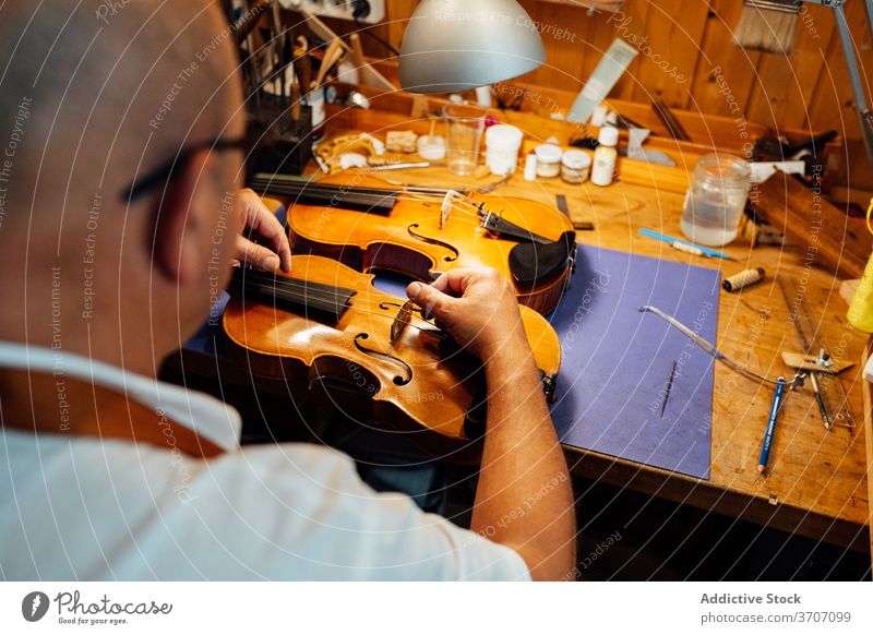 Geigenbauer beim Einstellen des Steges in der Werkstatt Arbeit Reparatur Kunsthandwerker Kunstgewerbler Brücke Schnur Instrument Zupfinstrumentenmacher Mann