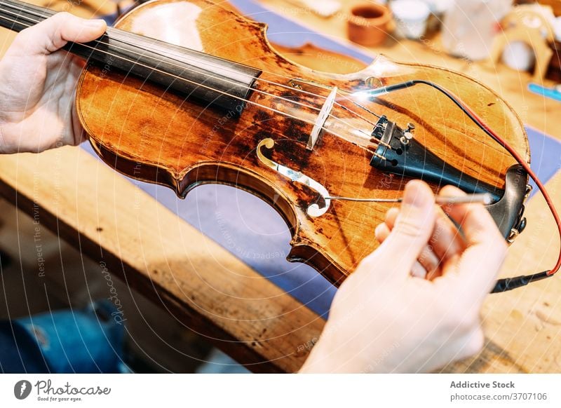 Anonymer Geigenbauer beim Einbau des Stimmstocks in die Geige Zupfinstrumentenmacher Klang einstecken installieren machen Instrument Kunstgewerbler Handwerk