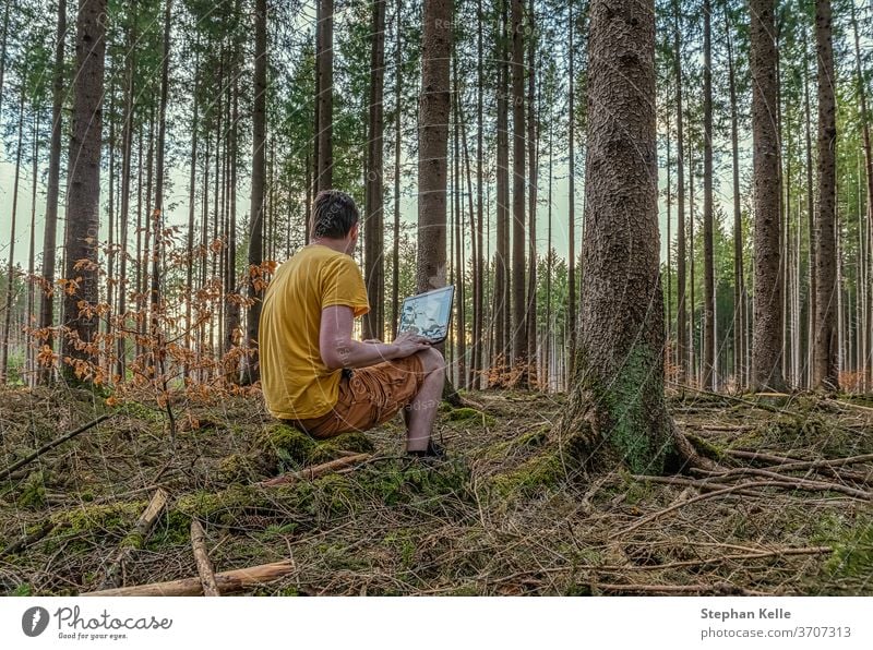 Ein Mann, der die Arbeit an der frischen Luft genießt, arbeitet mit seinem Laptop in einem natürlich aussehenden Wald. arbeiten modern gemütlich Büro frei