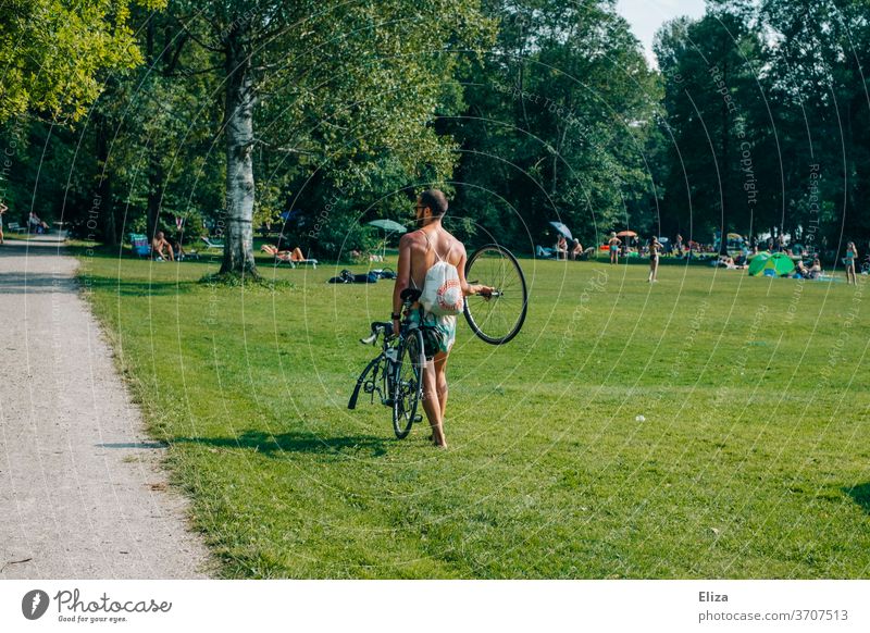 Ein Mann trägt sein Fahrrad, weil es einen Platten hat platten tragen Panne kaputt zu fuß Fußgänger Sommer Ausflug Mensch Pech Wiese Sonnenschein Park Weg stark