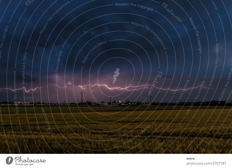 Gewitterstimmung mit Blitzen über Weizenfeldern bei bewölktem Himmel und Blick auf Inningen bei Augsburg Ansicht Atmosphäre bewölkter Himmel Textfreiraum dunkel