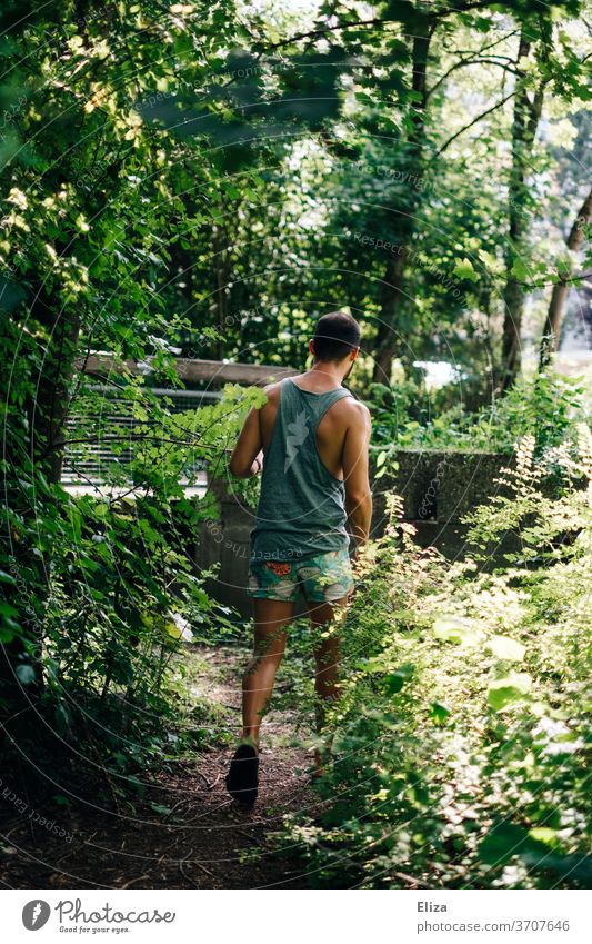 Mann von hinten in Sommerkleidung der eine Abkürzung durch das Gebüsch nimmt Pfad Natur gehen st sommerlich kurze Hose muskulös Tanktop Muscleshirt braunhaarig