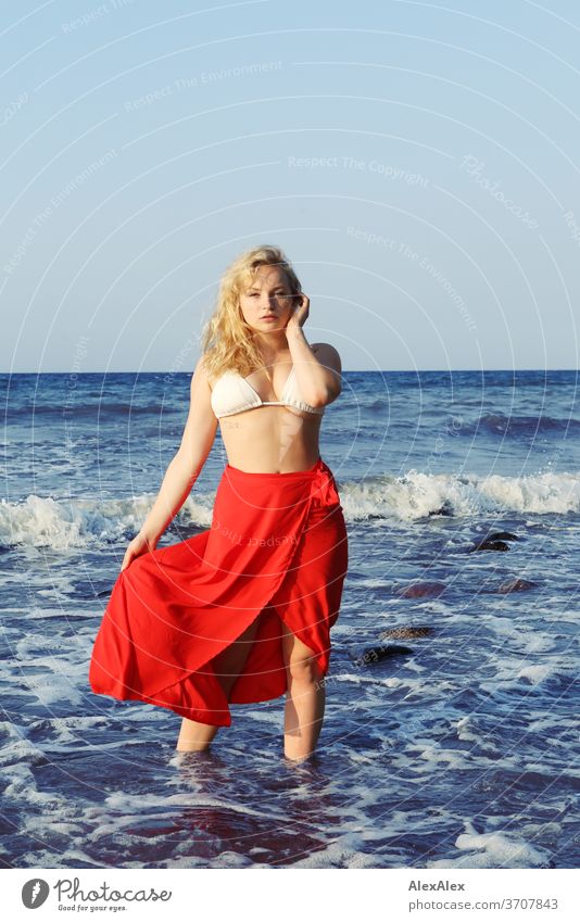 Portrait einer jungen, blonden Frau mit rotem Rock und Bikini- Top in der Ostsee junge Frau Mädchen 18-20 Jahre schlank schön lockig sinnlich natürlich