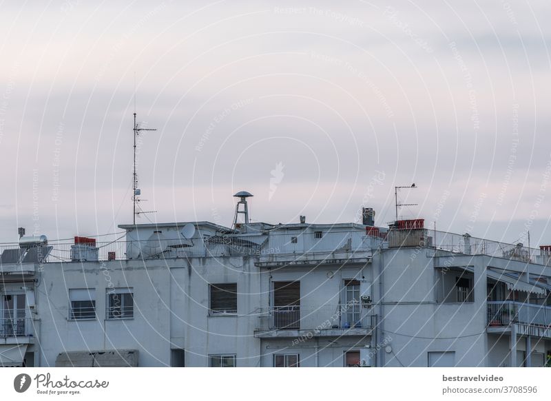 Kriegs-Luftangriffssirene auf dem Dach von Wohngebäuden. Abendansicht einer alten, pilzförmigen Angriffswarnsirene zwischen Antennen und Satellitenschüsseln auf dem Dach von Stadthäusern in Thessaloniki, Griechenland.