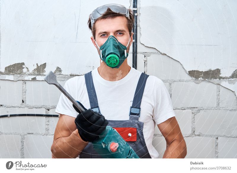 Renovierungskonzept. Mann in Bauarbeiteruniform mit Bohrhammer Reparaturen im Raum durchführen bohren Heimwerker Schutz Bauherr Konstruktion männlich Wand