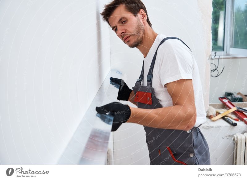 Renovierungskonzept. Männlicher Arbeiter verputzt eine Wand mit einem langen Spachtel verputzen Mann Werkzeug Stuck Industrie manuell Reparatur Konstruktion