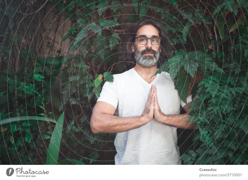 Mann in weiß mit langen grauen Haaren und Brille steht auf einem Garten mit seinen Händen zusammen in der Meditation hinduistisch chakra meditierend beten