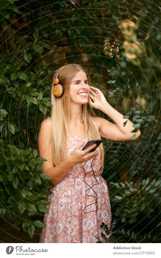 Glückliche junge Frau hört Musik im Garten zuhören Smartphone Kopfhörer heiter Lachen Spaß haben genießen blond Sommer Laubwerk Apparatur Gerät Lifestyle Freude
