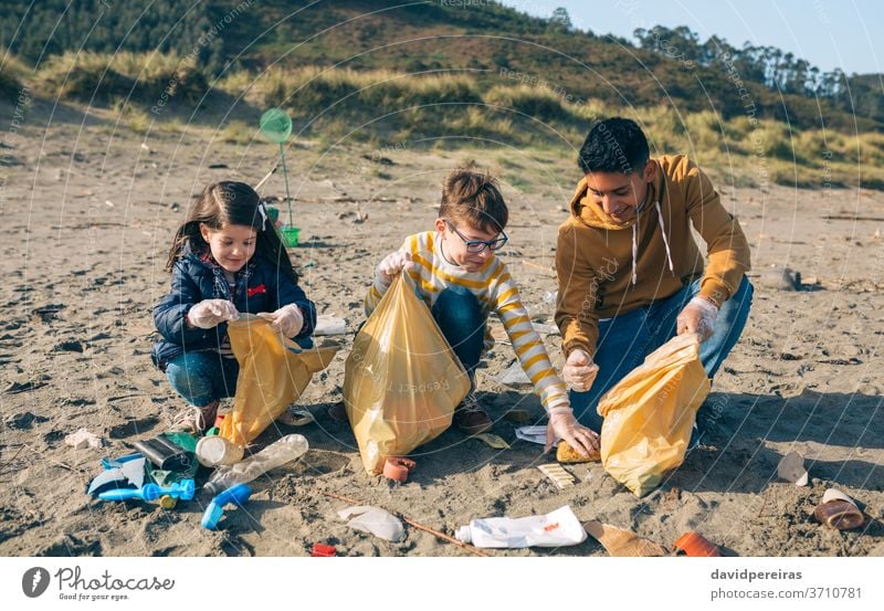 Junge Freiwillige reinigen den Strand jung Menschengruppe Reinigen Freiwilligenarbeit Lager Müllsäcke Lächeln abholend Umweltbewusstsein Werkzeuge Kind heiter
