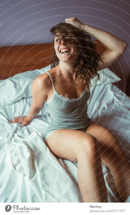 Von oben junge Frau, die mit offenen Augen und Haaren im Gesicht auf dem Bett sitzt und am Morgen lacht. schön zu Hause im Schlafzimmer bleiben Lifestyle Pyjama