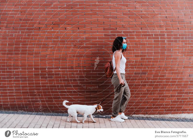 junge Frau, die mit Schutzmaske im Freien spazieren geht, daneben süßer Jack-Russell-Hund. Neues normales Konzept Straße neue Normale jack russell Haustier
