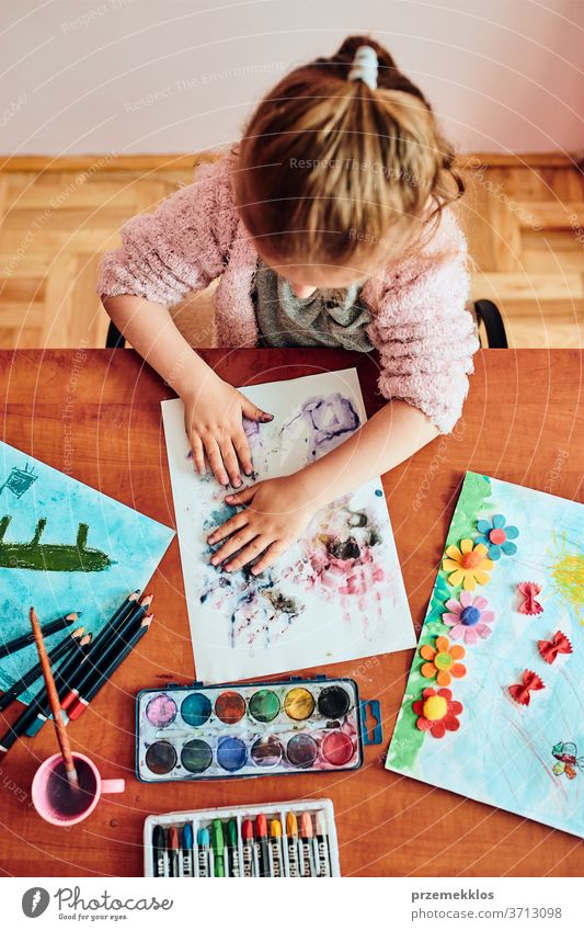 Kleines Mädchen im Vorschulalter, das mit bunten Farben und Buntstiften ein Bild malt. Kind, das während eines Kunstunterrichts im Klassenzimmer Spaß beim Malen eines Bildes hat