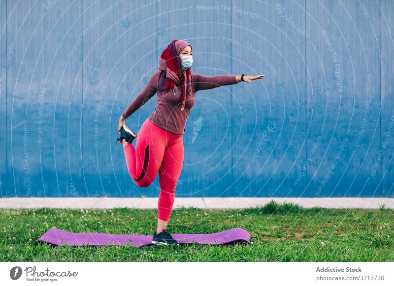 Frau beim Training im Park Aufwärmen Dehnung Sportlerin Hijab muslimisch Unterlage Athlet ethnisch arabisch medizinisch Mundschutz behüten Coronavirus COVID