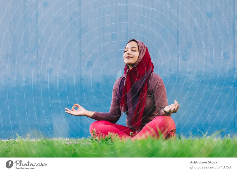 Muslimische Frau meditiert in Lotus-Pose meditieren Yoga Park üben Asana Achtsamkeit Stressabbau padmasana arabisch ethnisch Hijab muslimisch Sportbekleidung