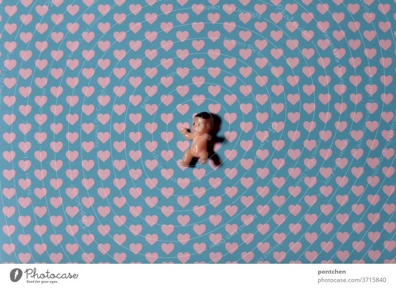 Ein miniatur babypuppe liegt auf einem Untergrund mit Herzen. Kinderwunsch, babyglück Baby herzen kinderwunsch schwanger Mensch Reproduktion künstlich liebe