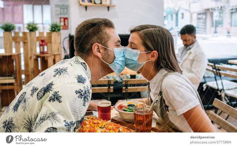 Paar, das sich mit Maske küsst und in einem Restaurant sitzt Küssen Mundschutz Coronavirus Liebe Nahaufnahme covid-19 Diner Kaffeehaus romantische Verabredung