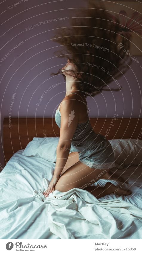 Brünette Frau, die auf dem Bett sitzend ihr Haar schüttelt. Bewegendes Foto. Schlafzimmer im Innenbereich Erholung träumend Kopfkissen sexy Freizeit LAZY