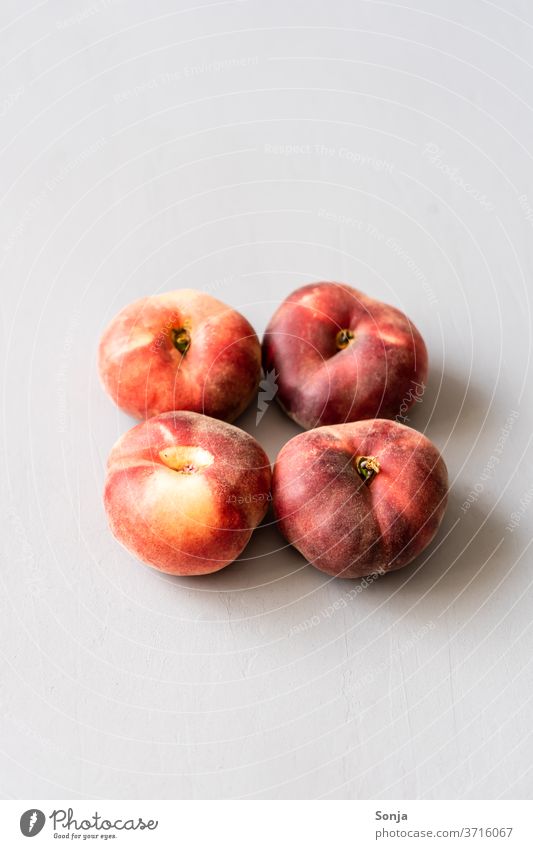 Vier rote flache Pfirsiche auf einem grauen Hintergrund in der Mitte Sommer Frucht roh saftig süß frisch reif Gesundheit geschmackvoll natürlich Nahaufnahme