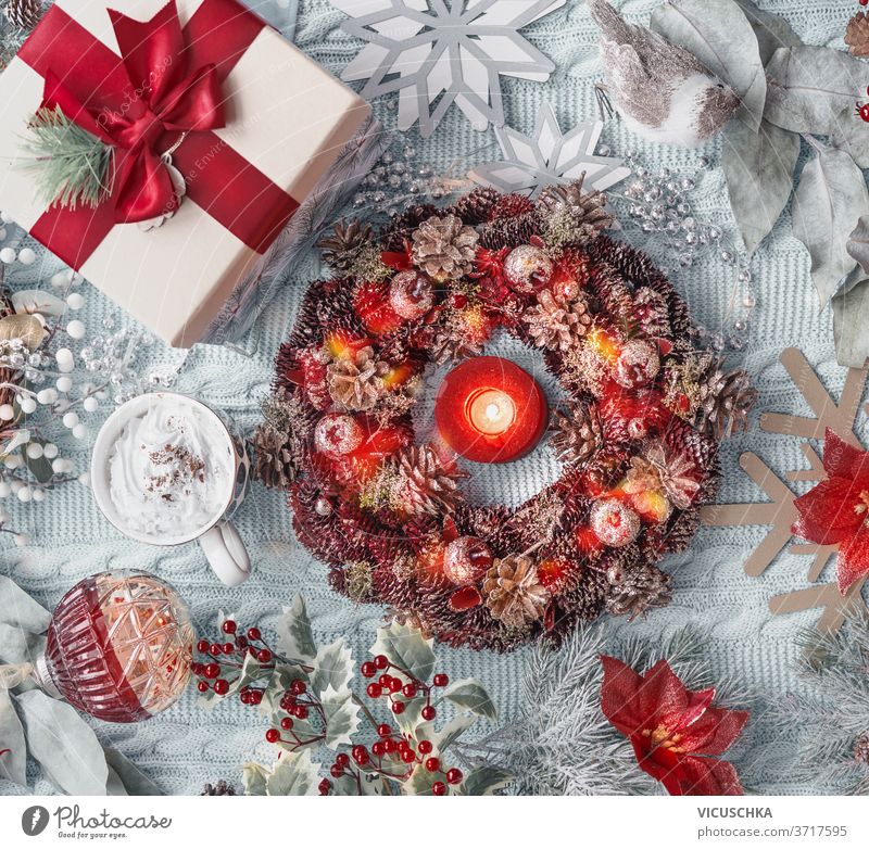 Weihnachtskonzept: Adventskranz, Geschenk, heiße Schokolade im Becher, Weihnachtsblume, Schneeflocken, Weihnachtskugeln und Stechpalme auf hellblauem Textilhintergrund. Ansicht von oben