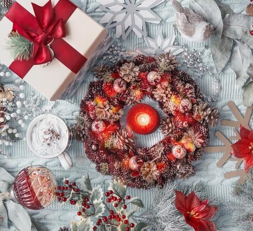 Weihnachtskonzept: Adventskranz, Geschenk, heiße Schokolade im Becher, Weihnachtsblume, Schneeflocken, Weihnachtskugeln und Stechpalme auf hellblauem Textilhintergrund. Ansicht von oben