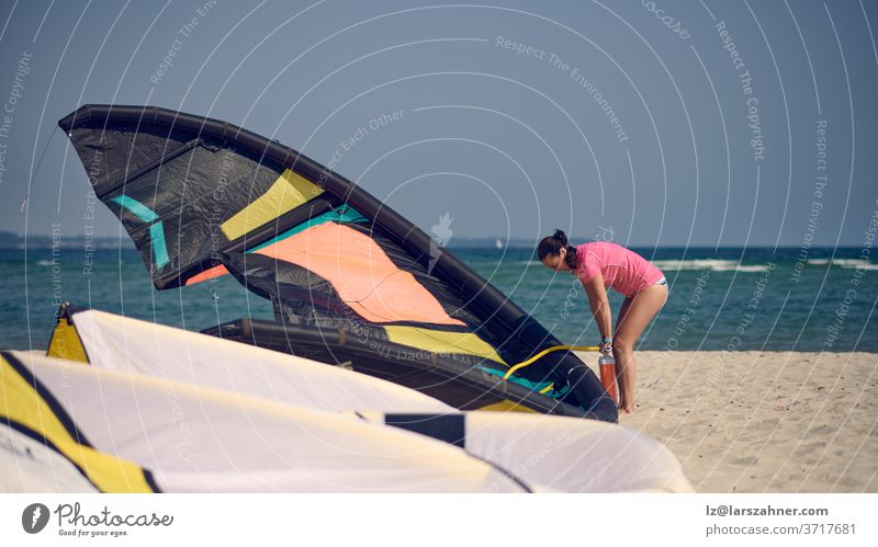 Frau mittleren Alters beim Aufpumpen eines Kitesurf-Drachens am Strand im Sommerurlaub bei heißem Sonnenschein mit Meereskulisse mittelgroß Milan Kitesurfen