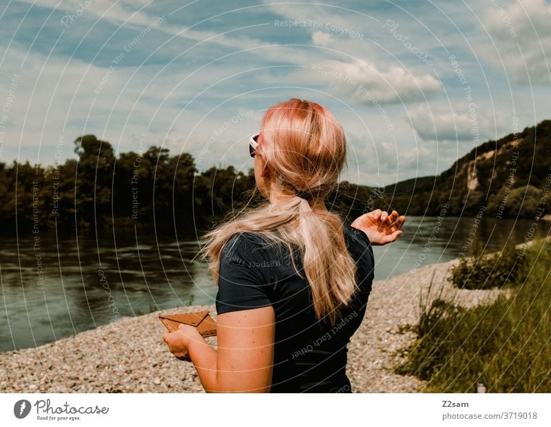 Junge Frau am Flußufer junge frau flußufer donau wasser landschaft grün sträucher natur blau himmel sport lange haare sportlich rückenansicht sonnebrille wolken