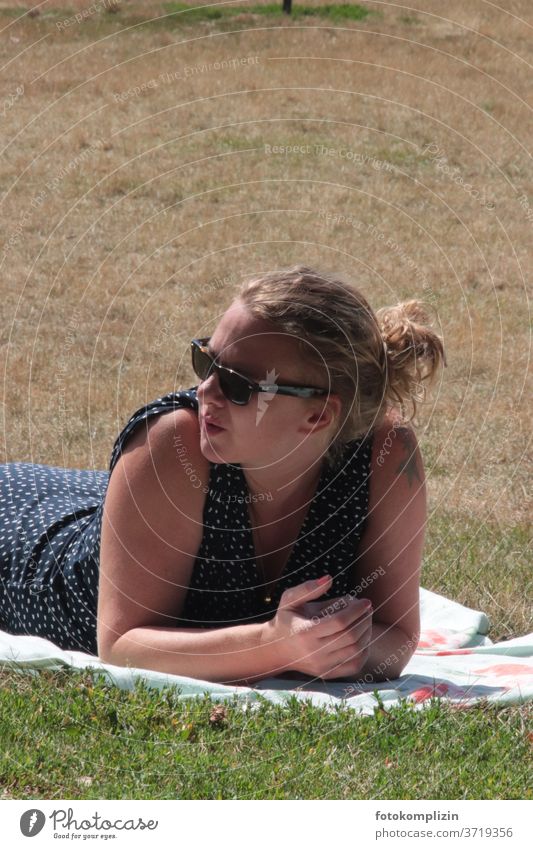Frau mit Sonnenbrille liegt auf trockener Wiese und blickt nach links Coolness Park schauen blicken Erwachsene chillen ernsthaft suchend nachdenklich Sommer