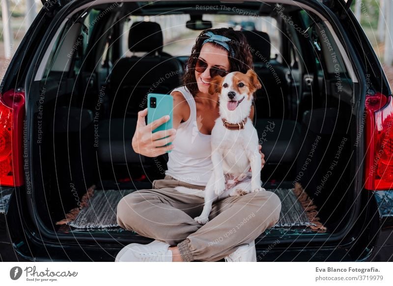 junge glückliche Frau in einem Auto, die sich mit ihrem süßen Hund vergnügt. Selbermachen mit dem Handy. Reisekonzept Technik & Technologie Selfie PKW reisen