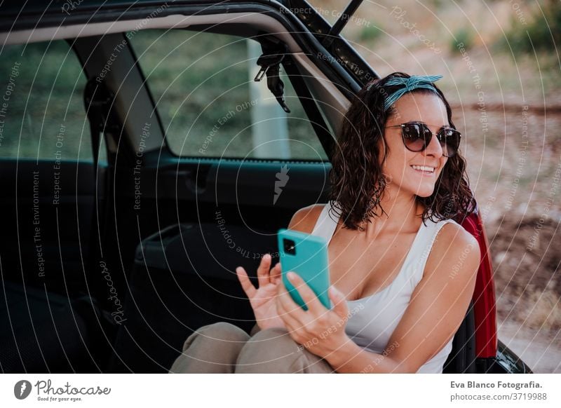 junge glückliche Frau in einem Auto, die ein Mobiltelefon benutzt. Reisekonzept PKW reisen Handy Glück Kaukasier Lächeln im Freien Warten Erwachsener
