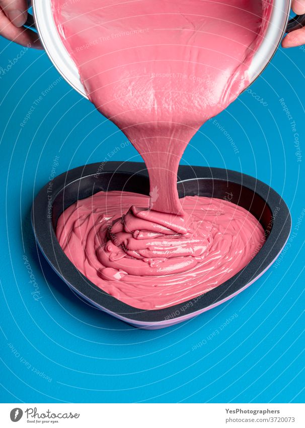 Geschmolzene rosa Schokolade wird in eine herzförmige Form gegossen. Rubinroter Schokoladentropfen Hintergrund Belgier blau Nahaufnahme Konditorei