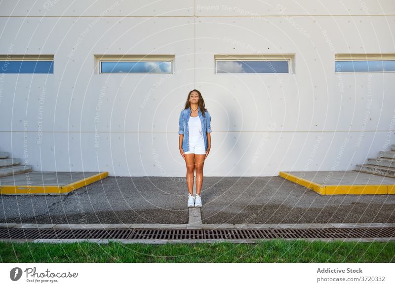 Frau in Sommerkleidung steht mit geschlossenen Augen auf einem Parkplatz Befriedigung Lebensstile Positivität Wiederherstellung Gelassenheit entspannt