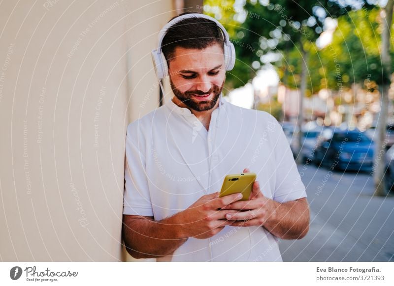 glücklicher junger Mann im Freien, der mit Handy und Headset Musik hört. Technologie und Lebensstil hören Technik & Technologie Großstadt urban Glück Lächeln