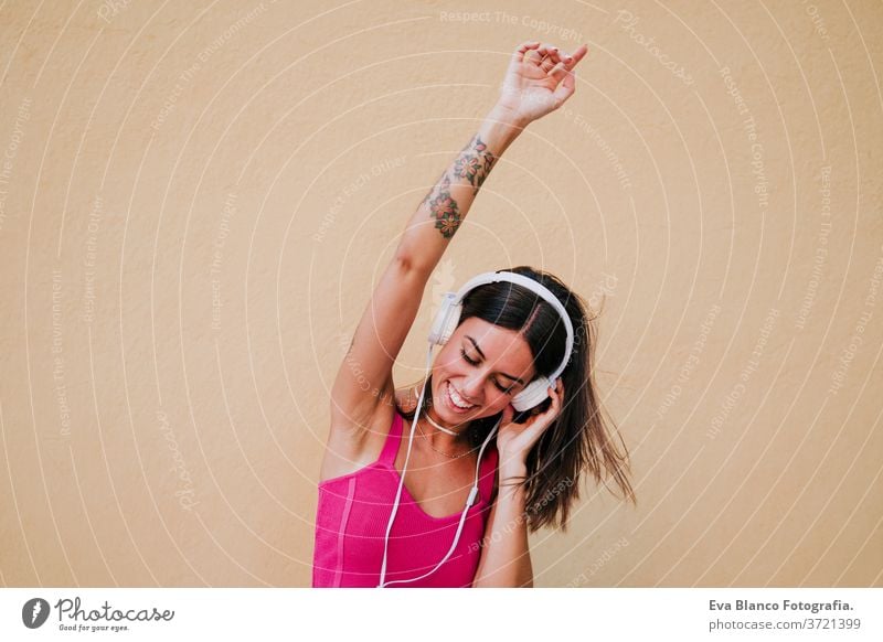 fröhliche junge Frau, die draußen tanzt und mit Handy und Headset Musik hört. Technologie und Lebensstil Musik hören Glück Tattoo Technik & Technologie